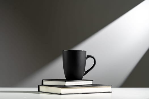 Black cup on books in sunlight on gray background
