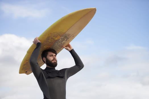 Man, surfboard and adventure at beach on holiday, weekend and sports for fitness in water. Male person, balance and cloudy sky on tropical island, wetsuit and travel on vacation or getaway for peace