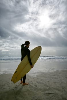 Man, surfboard and adventure at beach on vacation, weekend and sports for fitness in water. Male person, back and cloudy sky for ocean waves, wetsuit and traveling on holiday or getaway for peace