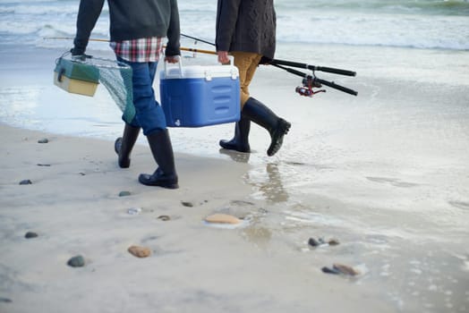 Closeup, walking and beach with fishermen, cooler box and activity with equipment or weekend break. People, ocean or friends with tools for hobby or early overcast morning with waves, sand or seaside