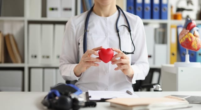 The doctor in the clinic holds a plastic model of the heart, close-up. Prevention of stroke and heart attack, diagnosis