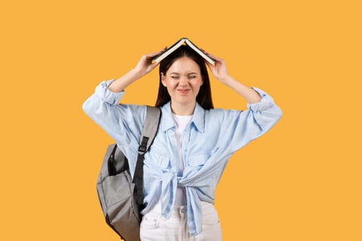Tired female student with book on head and backpack