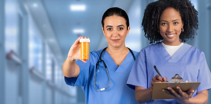 Two attentive women nurses in blue scrubs, one holding medication