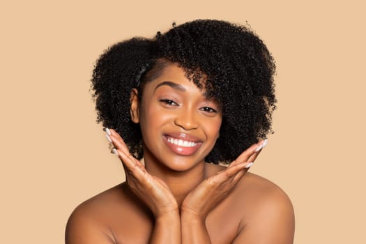 Joyful black woman with curly hair smiling with hands near face