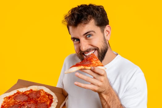 Cheerful guy bites into a slice of pizza in studio