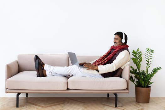 Relaxed mature indian man using laptop and headset