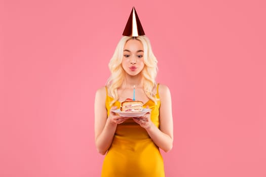 Woman in party hat blowing out candle on cake