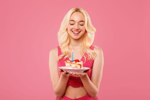 Blissful young woman with birthday cake, eyes closed in wish