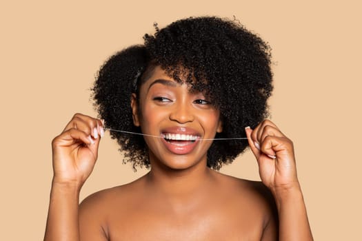 Joyful black woman with curly hair flossing her teeth
