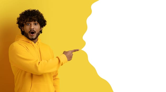 Excited indian guy pointing at free space on yellow backdrop