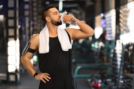 Fitness Lifestyle. Sporty young man drinking water from bottle at gym