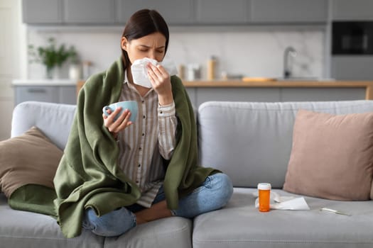 Ill woman with cold sitting on couch with medicine