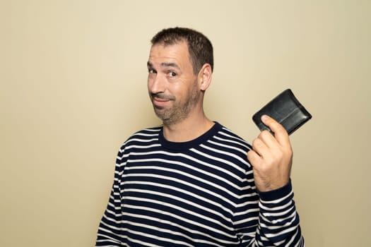 Hispanic man with beard in his 40s wearing a striped sweater smiling and proudly showing his wallet isolated on beige studio background