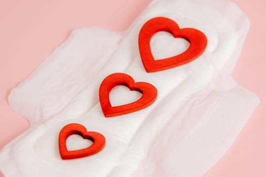 Women's sanitary pad with three red hearts on a pink background.