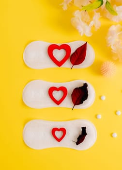 Women's sanitary pad with red hearts, pills and virus ball on a yellow background.