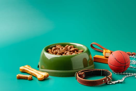Dog dry food in bowl, toy ball and leash on green background