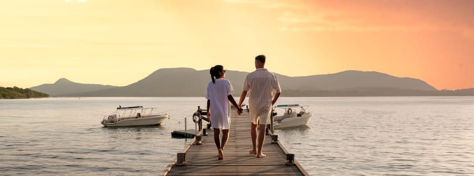 couple walking on a wooden pier in the ocean at sunset in Thailand