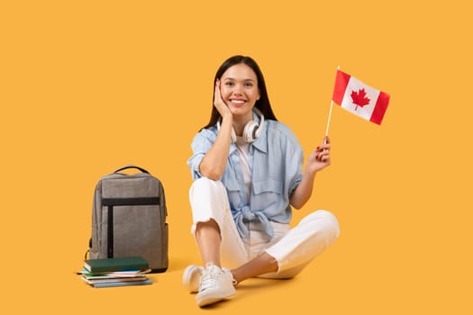 Content lady student with Canadian flag and headphones on yellow background