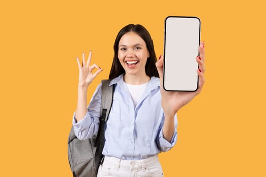 Happy female student showing cellphone with OK sign