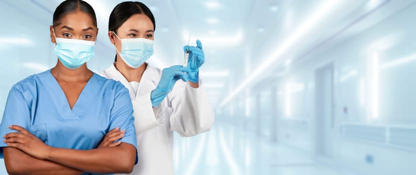 Two female healthcare workers in a clinical setting, one with arms crossed in a blue scrub