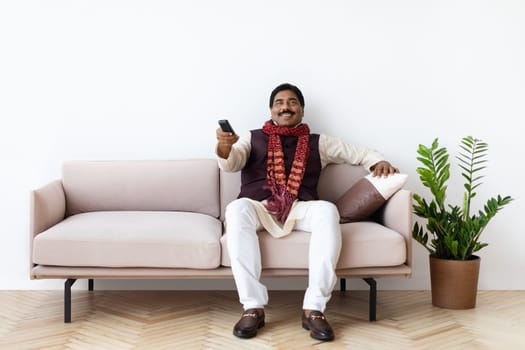Happy mature indian man watching TV in living room