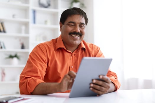 Cheerful middle aged indian man typing on tablet, planning startup