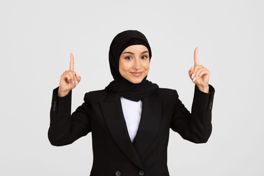 Smiling young businesswoman in hijab pointing upwards