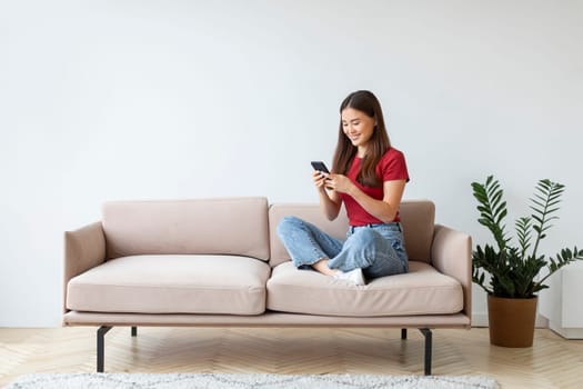 Young Asian Woman Using Smartphone While Resting On Sofa At Home