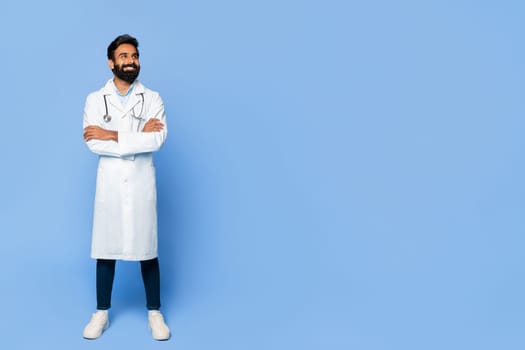 Happy indian doctor with folded arms on blue background, free space