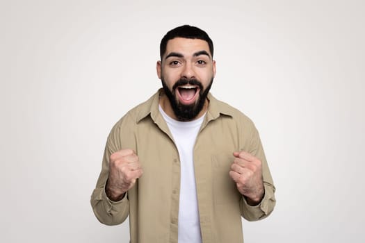 Happy shocked handsome young latin man winner with beard in casual with open mouth