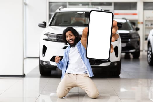 Emotional indian guy standing on knees and showing smartphone