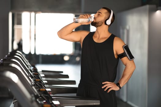 Handsome Young Male Athlete Drinking Water While Training At Treadmill At Gym,