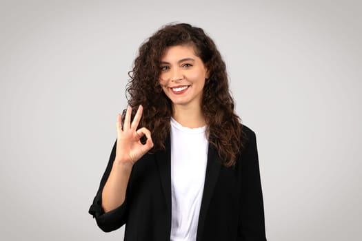 European businesswoman in black suit making an OK hand sign with confident smile, suggesting success and approval