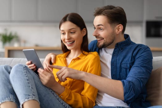 Excited caucasian spouses using digital tablet on the couch