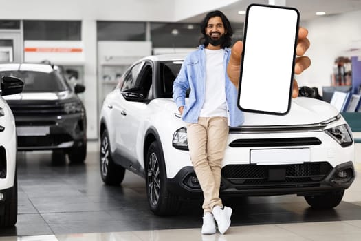 Emotional young eastern man choosing new car, showing mobile phone