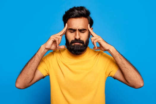 Indian man in yellow feeling stressed with headache