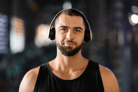 Portrait Of Smiling Athletic Young Man Wearing Wireless Headphones Posing In Gym