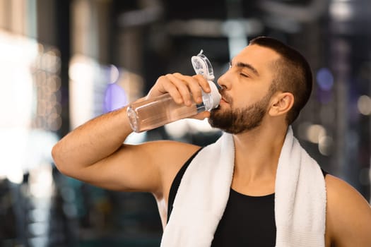Sporty young man drinking water from bottle after training at modern gym