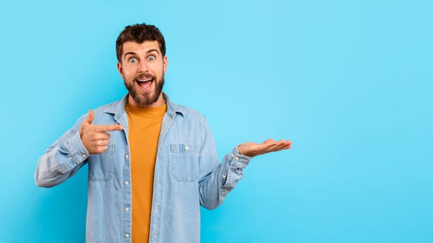 Excited guy points at his hand showing copy space, studio