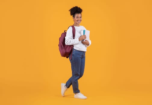 Cheerful young black student woman carrying backpack and workbooks