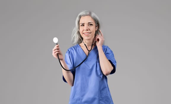 Happy nurse lady holding stethoscope listening heartbeat over gray background
