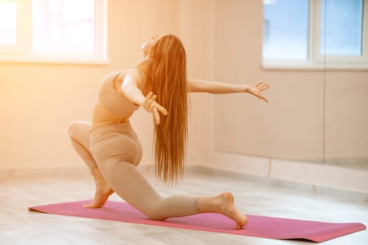 Girl does yoga. Young woman practices asanas on a beige one ton background.