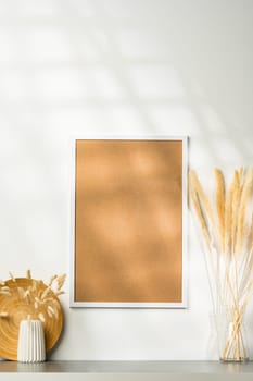 White blank photo frame with dry flowers in vase against white wall