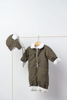 Baby gray quilted winter overalls on hanger against white wall