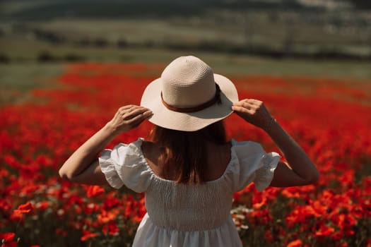 Field poppies woman. Happy woman in a white dress and hat stand through a blooming field of poppy raised her hands up. Field of blooming poppies.