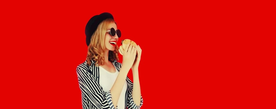 Portrait of happy cheerful young woman having fun with burger fast food isolated on red studio background