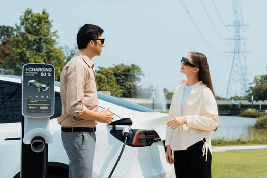 Young couple recharge EV car battery at charging station. Expedient