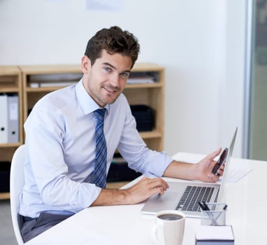 Portrait, office and businessman with phone, laptop and coffee at startup with technology. Smile, online and business analyst at desk with computer, smartphone and internet connection for networking