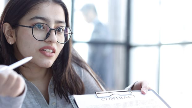A young woman with glasses in the office discusses signing a contract