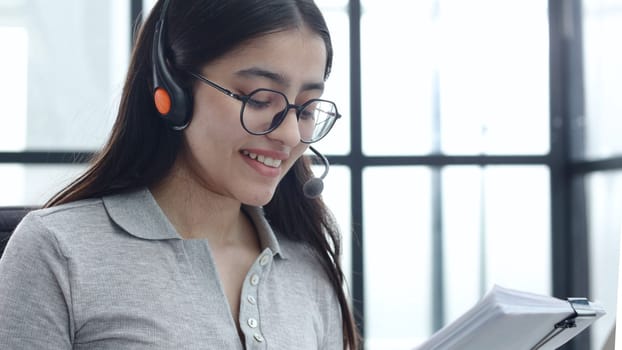 A young woman in close-up with glasses and headphones works in a call center